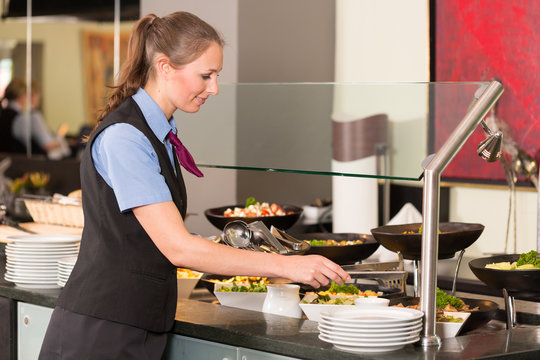 Waitress or catering professional putting food into buffet