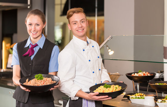 cook and waitress from catering service posing in front of buffe