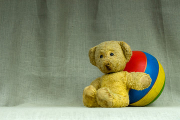 Yellow vintage teddy bear with a striped ball