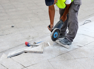 Fototapeta premium Worker cutting granite tiles for paving the street