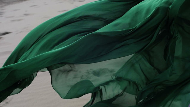 Beauty Girl in green dress running on sand dune while wind