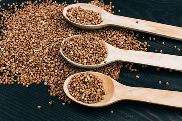 buckwheat groats and wooden spoon on the black table