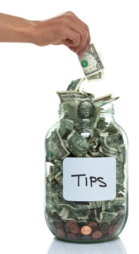 Hand putting money into a savings jar with a white tip label