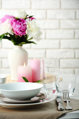 Beautiful table setting with flowers in vase on brick wall background