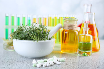 Herbs in mortar, test tubes and pills,  on table, on light background