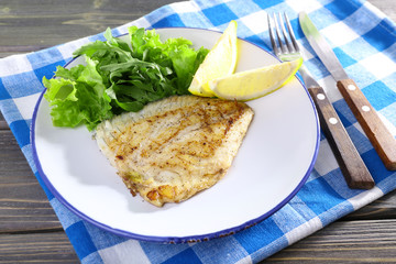 Dish of fish fillet with lettuce and lemon on table close up