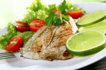 Dish of fish fillet with salad and lime on plate close up