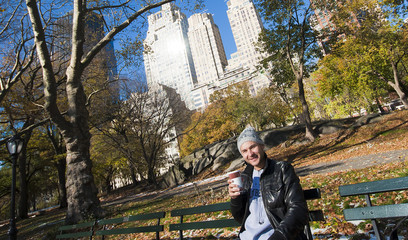 Young man smiling and drinking coffee on bench in Central Park N