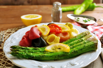 Roasted asparagus and tasty colorful pasta with vegetables on plate on wooden table background