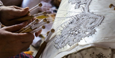 artist rapidly creating lace with bobbins and white thread