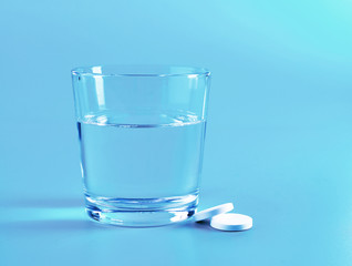 Glass of water and pills on blue background