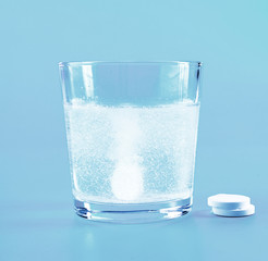 Glass of water and pills on blue background