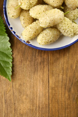Ripe mulberries with green leaves on table close up