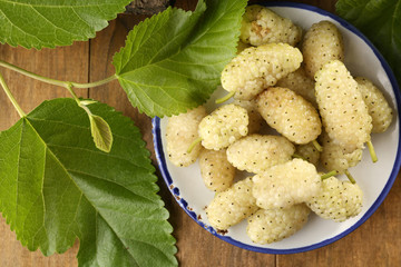 Ripe mulberries with green leaves on table close up