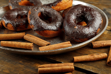 Delicious doughnuts with chocolate icing and cinnamon on table close up