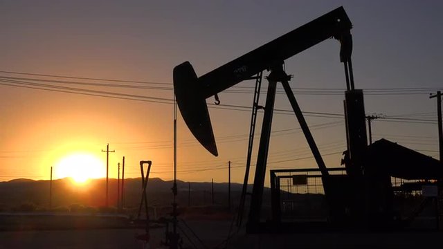 An oil derrick pumps against the sunset.