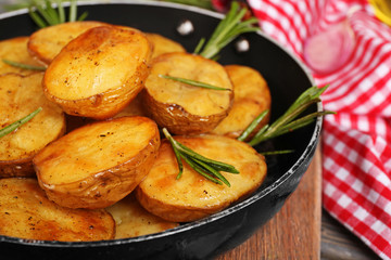 Delicious baked potato with rosemary in frying pan on table close up