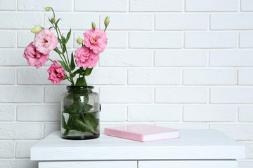 Beautiful flowers in vase on brick wall background