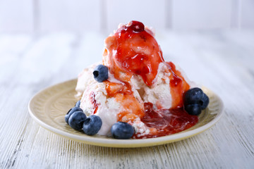 Delicious ice cream with fresh frozen berries and sauce, on color wooden background