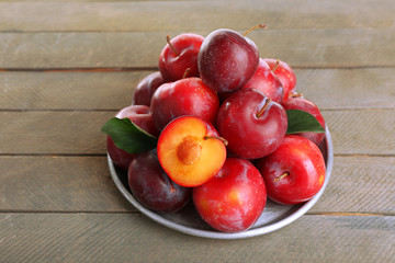 Ripe plums in metal plate on wooden background
