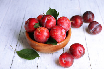Ripe plums in bowl on wooden background