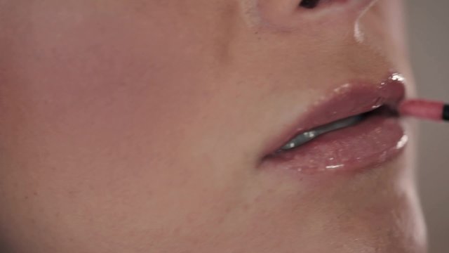 Close-up of woman's lips as she puts lipstick on with brush