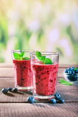 Glasses of berry smoothie on wooden table on blurred background