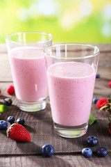 Glasses of berry smoothie on wooden table on blurred background