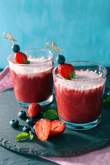 Glasses of berry smoothie on wooden table on blue wall background