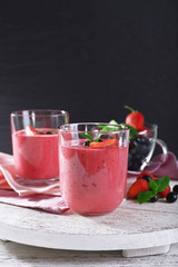 Glasses of berry smoothie on wooden table on dark background