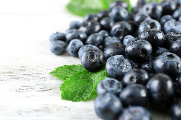 Tasty ripe blueberries with green leaves on wooden table close up