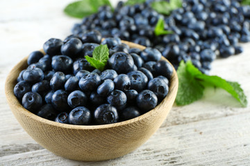 Tasty ripe blueberries with mint in bowl on table close up