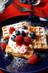 Sweet homemade waffles with forest berries and cream on plate, on dark wooden background