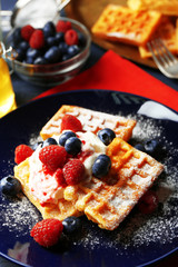 Sweet homemade waffles with forest berries and cream on plate, on dark wooden background