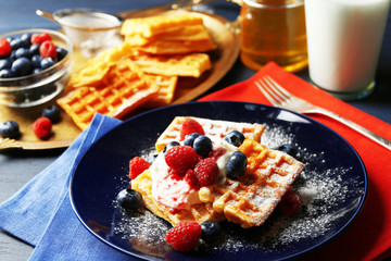 Sweet homemade waffles with forest berries and cream on plate, on dark wooden background