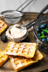 Sweet homemade waffles and blueberries on tray, on color wooden background
