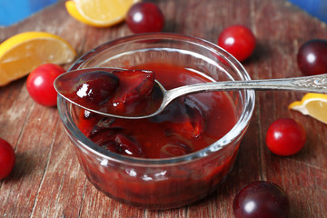 Tasty homemade plum jam in glass saucer on wooden background
