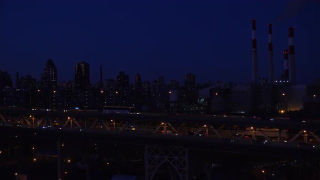 Night shot across the Queensboro Bridge with vehicle traffic and New York Manhattan skyline in background.
