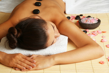 Fototapeta na wymiar Young woman with pebbles on her back on massage table in beauty spa salon