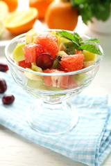 Fruit salad in glass bowl, on light wooden background