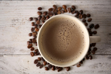 Cup of coffee with beans on wooden table, top view