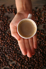 Female hand holding cup of coffee with foam over grains, top view