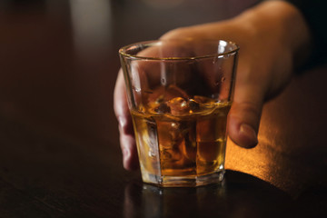 Whiskey glass tumbler in male hand on bar counter