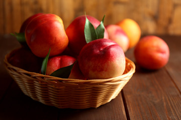 Fresh peaches in wicker basket on wooden background