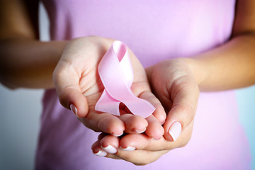 Pink ribbon in woman's hands close up