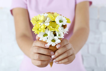 Woman's hand holding wild flowers in wafer on light wall background