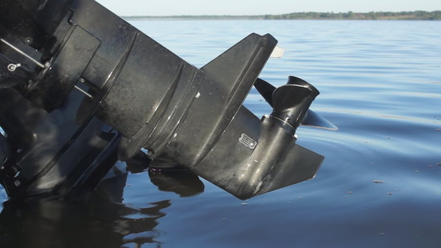A black outboard motor with propeller, hangs off a fishing boat, but above the water, as small, quiet waves roll by on a large lake.