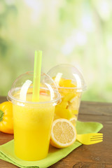Yellow vegetable and fruit salad and healthy fresh drink in plastic cups on wooden  table, on bright background. Colorful diet concept
