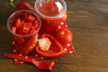 Red vegetable and fruit salad and healthy fresh drink in plastic cups on wooden background. Colorful diet concept
