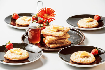 Toasted crumpets with honey drizzled over them and strawberries in the background.